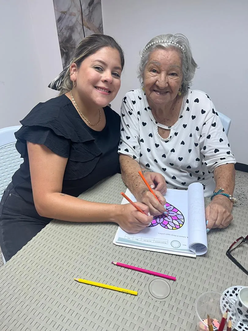 Cuidadora de Cuidadoras de Amor acompañando a una señora mayor en una actividad de colorear, en la sede de Barquisimeto